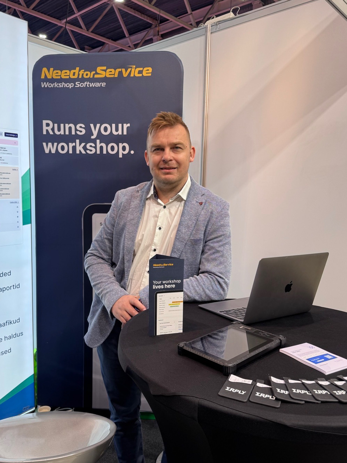 Kristo at the Need for Service booth — the workshop software banner behind him reads 'Runs your workshop'